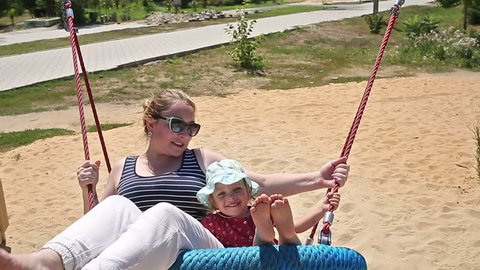 Mother and daughter ride a big swing sunny summer day in the park. The concept of a happy childhood and motherhood.