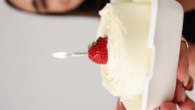 close-up of a cake with strawberries and a candle. the girl holds a festive cake in her hands on a white background. vertical video. birthday celebration