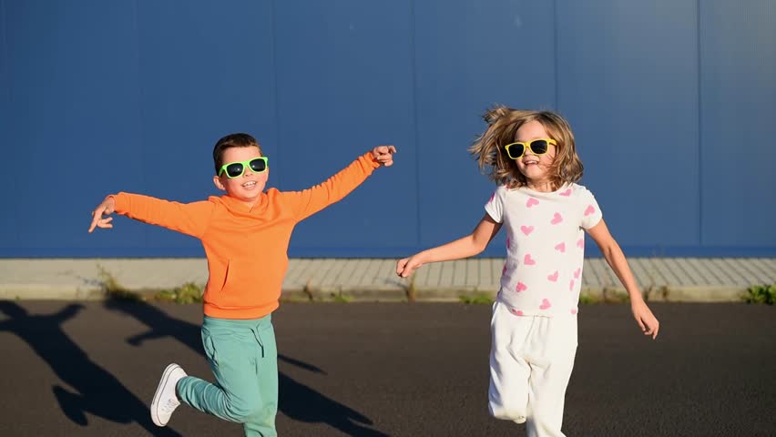 Cute happy European children boy and girl from Ukraine in bright clothes and white are dancing and having fun outside on the street, against a blue wall