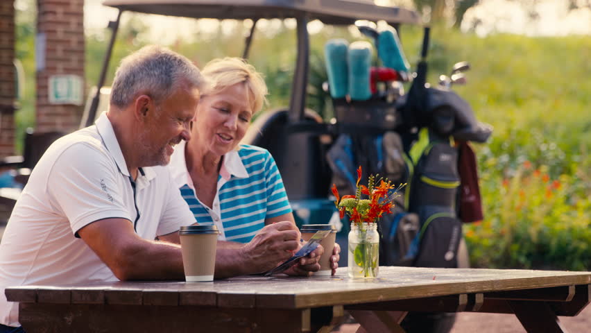 Senior retired couple sitting having coffee after round of golf looking at score card together - shot in slow motion Royalty-Free Stock Footage #1109448227
