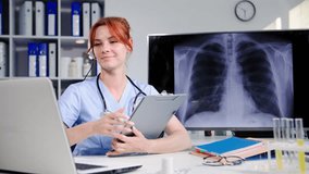 young female doctor communicates with patients via video conference on a laptop using headset and shows results of an x-ray while sitting in medical office