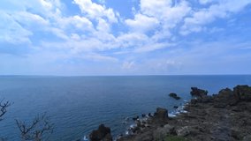 Blue sky and white clouds, waves lapping against the rocks on the coast, time-lapse video of clouds flowing in the sky.