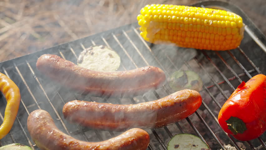Sausages are grilled on grill with fresh vegetables yellow corn, red pepper.  in nature camping in summer at sunset in pine forest. Go Everywhere. Camping family in pine forest. Lifestyle. Travel