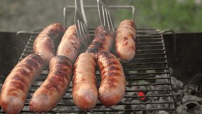 Grilled sausages. Cook man preparing grilling food bbq. Barbecue with smoke, flame outdoors. Tasty juicy german bratwurst. Charcoal kettle grill outside in backyard. Family summer vacation. Close-up