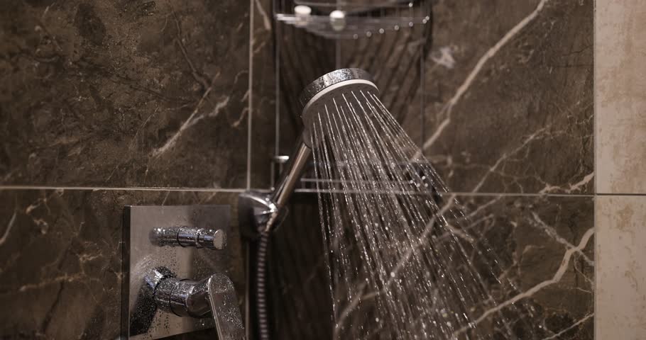 Water spurts out of colander attached on wall of shower stall in bathroom. Woman turns off faucet with strong jet of water Royalty-Free Stock Footage #1109454947