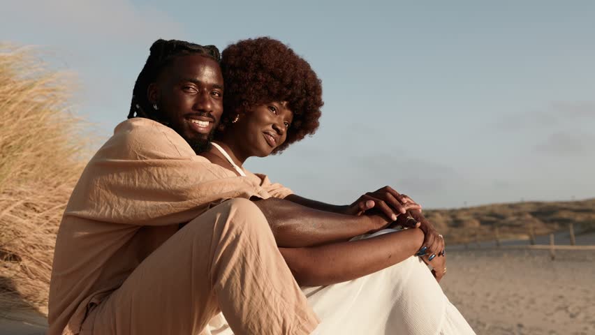 In a serene sunset setting, a stylish African couple shares a romantic moment on a sandy dune. Their deep love is evident as the black man embraces the afro woman, sharing laughter Royalty-Free Stock Footage #1109459565