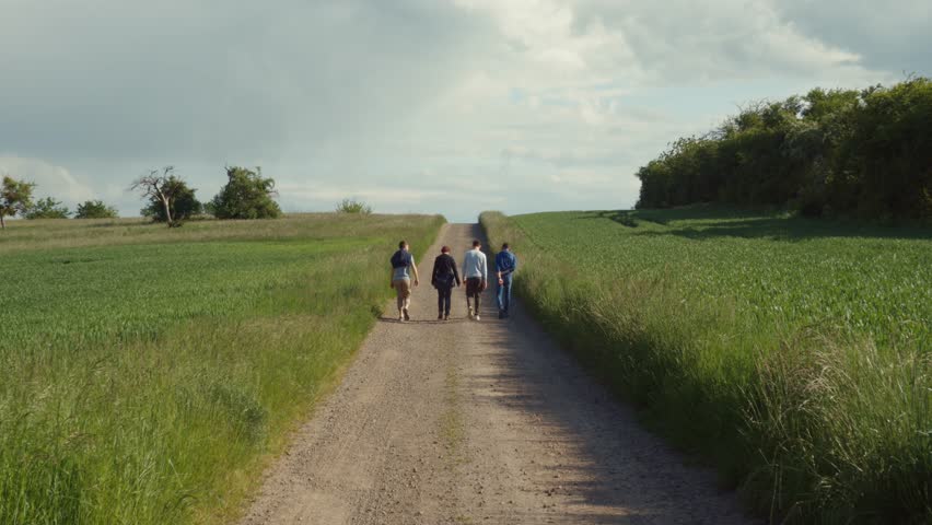 People walk on a dirt track through grass fields in slow motion. 