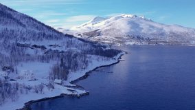 Snow covered mountain range on coastline in winter, Norway. Surroundings of town Tromso. Panoramic aerial view landscape of nordic snow cowered mountains, houses and ocean. Troms county, Fjordgard - Powered by Shutterstock - Get 15% off with code: PIKWIZARD15