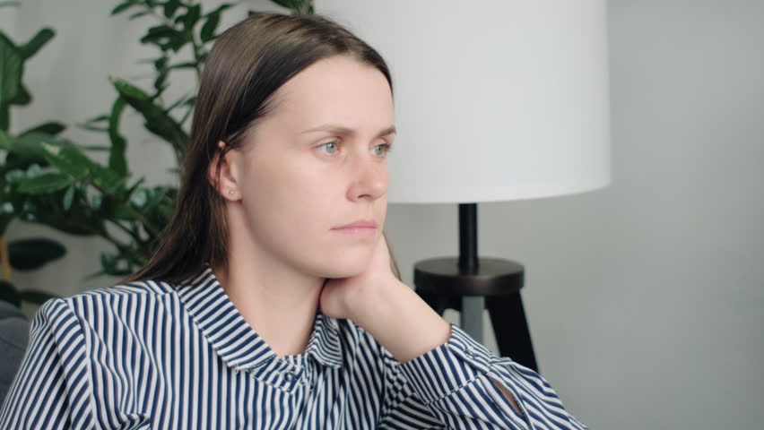 Close up of sad young lady sitting on sofa deep in unhappy thoughts, looking away leaning head on hand, have melancholic mood, thinks on quarrel with beloved man, feel boredom on weekend alone at home Royalty-Free Stock Footage #1109461387