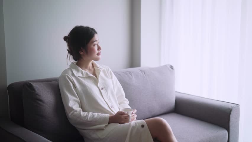 a young Asian woman relaxing drinking the winter morning coffee or tea on couch in modern living room at home