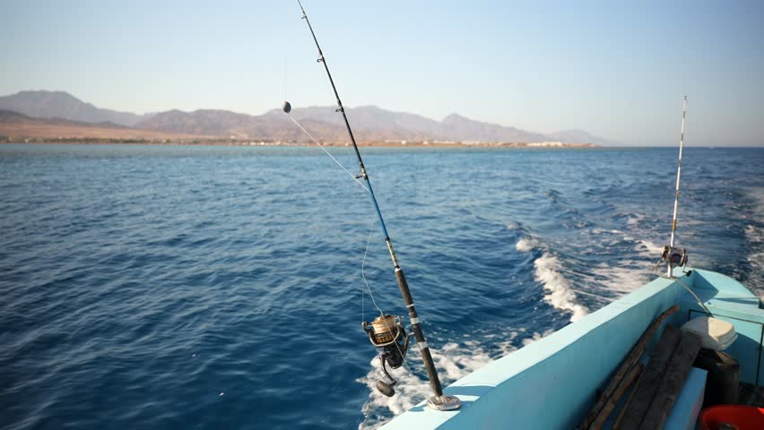 Two fishing rods in holders on a moving motor boat in the Red sea. Mountains on the coast in the background. Dahab, Egypt