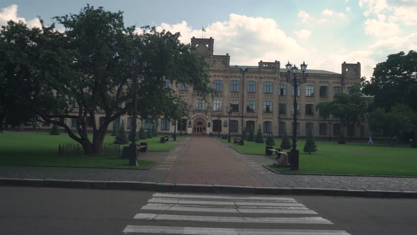 a slow walk along the alley of red paving stones to the old building of the Kyiv University. On the sides there is a well-groomed, trimmed lawn and trees. Ukrainian flag on the roof of the building