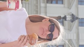 A young woman with a croissant and a cup of coffee on a city walk. Vertical video.