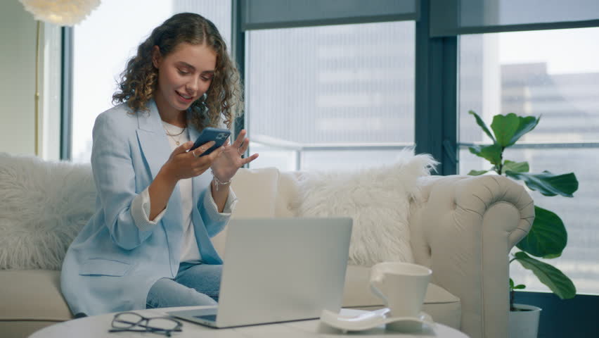 Smiling young woman using smartphone device at home. Positive millennial girl holding cell phone. Attractive blogger subscribing social media, ordering products online or buying on internet in app 4K Royalty-Free Stock Footage #1109482759