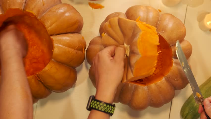 Close-up, woman and man hands vigorously removing core from pumpkin, preparing it to create Jack-O-Lantern. Pumpkins for during Happy holiday Halloween background, on table top view.