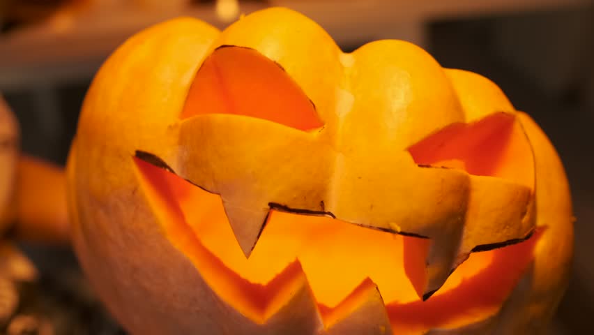 Сlose-up of carved Jack-o'-lantern spinning in his hands against blurred of flickering candles and glowing garlands late at night. Festive mood during Halloween 31 October background.  Royalty-Free Stock Footage #1109492357