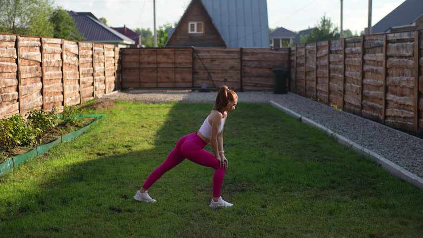 Athletic young woman in sportwear training on house garden lawn performing squat enjoying healthy lifestyle physical activity. Sports redhead female doing outdoor training outdoors, slow motion. Royalty-Free Stock Footage #1109494481