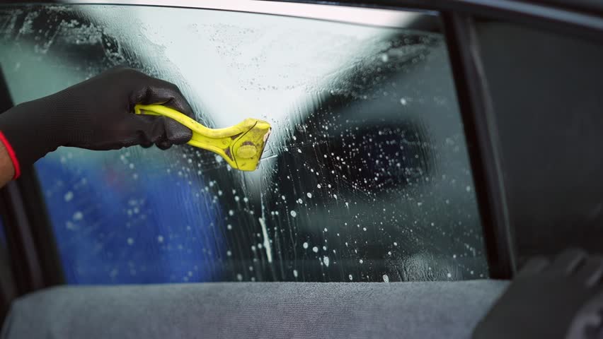 Technician uses tools to install car window tint film Royalty-Free Stock Footage #1109496195