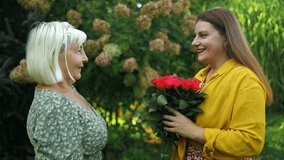 Happy mother's day. Young daughter is congratulating mom and giving her flowers roses at a backyard party at home. Mum and girl smiling and hugging. Family holiday and togetherness outdoors - Powered by Shutterstock - Get 15% off with code: PIKWIZARD15