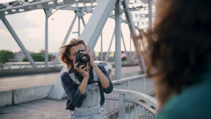 Young woman taking pictures of young man by busy bridge