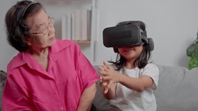 Smiling overjoyed mature grandmother with little granddaughter using VR on cozy couch. Happy mature granny and small grandchild play education videos tablet. Education online, mature joy concept.