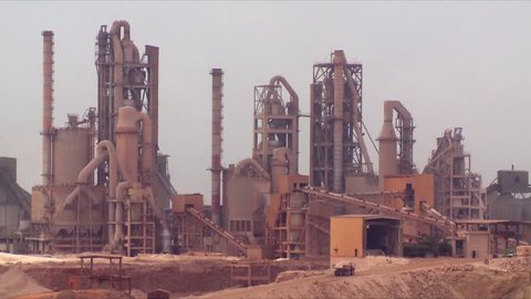 A static close up of a working cement factory in an industrial area in Salalah, Oman, showing moving trucks