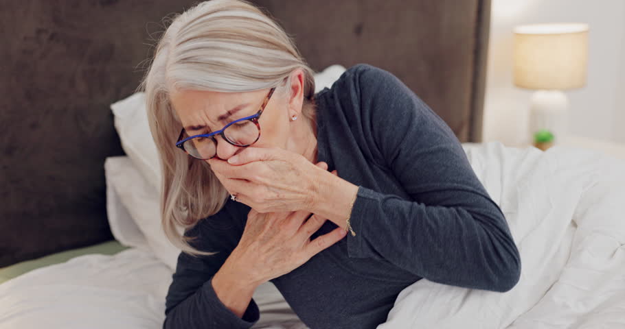 Senior woman coughing for chest pain, flu or sickness in her modern retirement home in morning. Medical, recovery and elderly female patient resting with cold or sickness in her bedroom in a house.