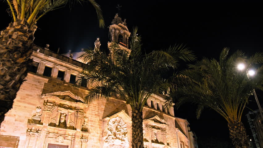 Night Catholic church Real Parroquia de los Santos Juanes Valencia with Palm trees. Long-standing Catholic church featuring a triangular bell tower topped with statues of saints at night in Spain Royalty-Free Stock Footage #1109517495