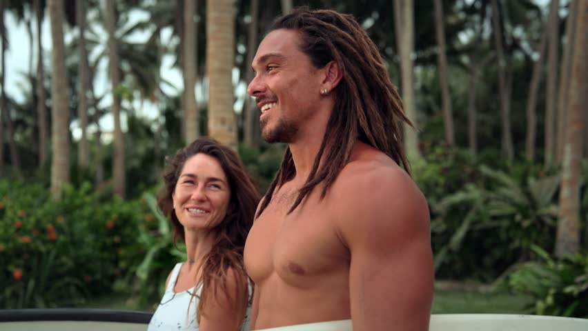 Couple Of People With Surf Boards Talking Happy In Green Nature Of Sea Beach. Ocean Surfers Moving With Surfboards To Playful Vacation Date. Relationship Inspiration In Man And Woman At Summer Travel
