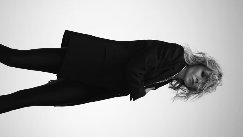 A beautiful woman with loose hair, in a jacket and beads, poses in the studio in a black and white video