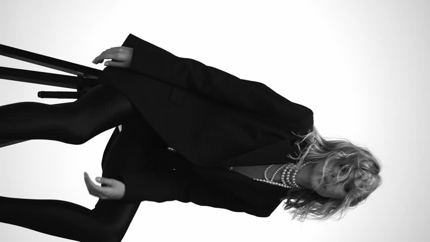 A beautiful woman with loose hair, in a jacket and beads, poses in the studio in a black and white video