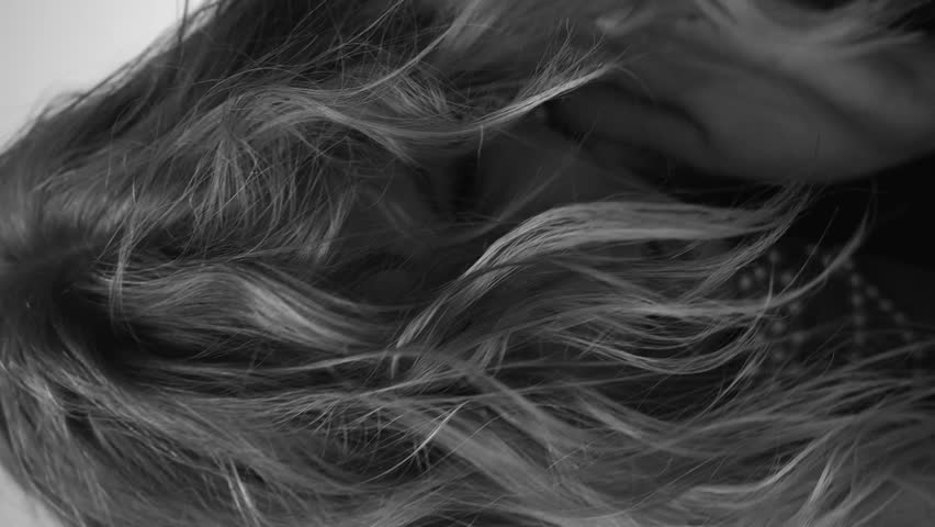 A beautiful woman with loose hair, in a jacket and beads, poses in the studio in a black and white video