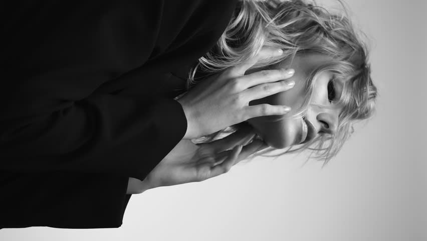 A beautiful woman with loose hair, in a jacket and beads, poses in the studio in a black and white video