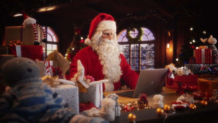 Arc Shot of Father Christmas Sitting and Using a Modern Laptop Computer. Santa is Browsing Online, Communicating with Clients, Managing a Successful Online Shopping Business with Gifts for Children Royalty-Free Stock Footage #1109535049