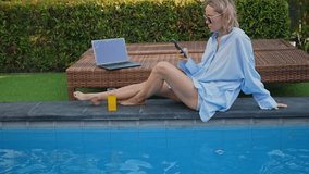 Female freelancer working near the swimming pool with laptop and smartphone at sunset time