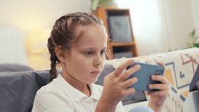 Medium close up of pre-teen girl playing game on smartphone while sitting alone in her room after school