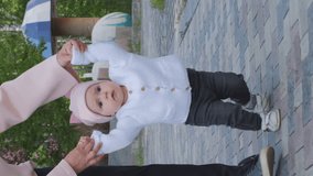 Vertical video. Young woman holding hands of her baby when walking, mother guiding her infant daughter with first steps, slow motion