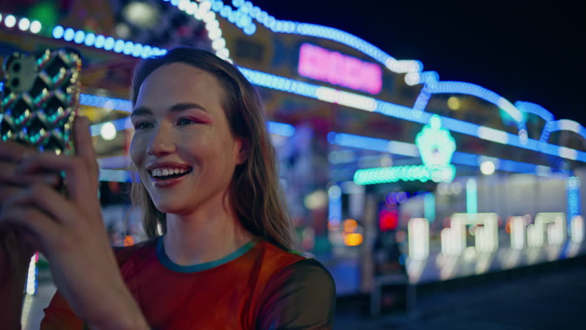 Teenage girl streaming smartphone video at funfair closeup. Excited blogger use mobile phone recording creating social media content. Happy smiling teenager enjoying weekend at amusement luna park