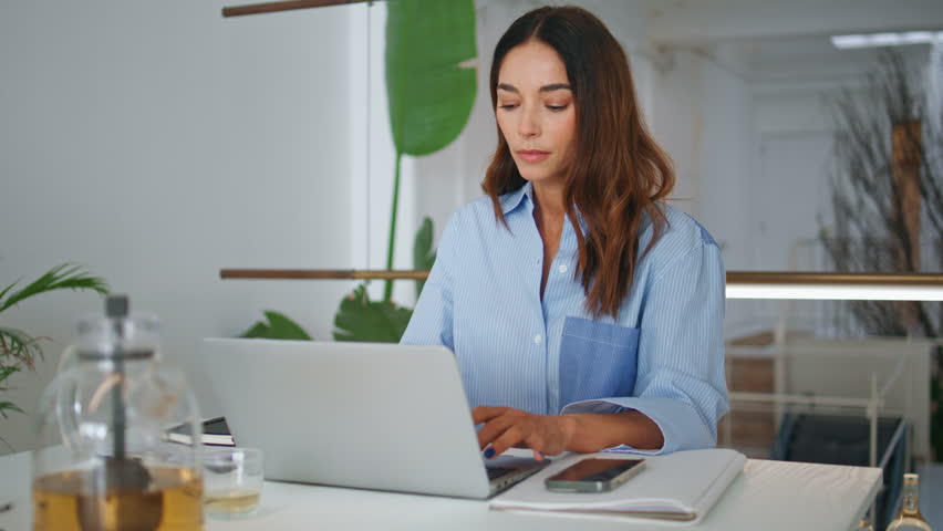 Attractive woman browsing laptop in contemporary office. Focused project manager typing computer analysing data. Successful businesswoman looking screen working in creative studio. Female ceo concept