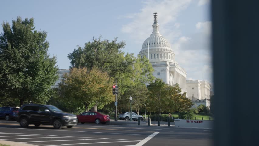 Slow motion view of Capital building holding congress house representatives and senators in Washington DC, including pedestrians, streets, and traffic during a bright, fall afternoon