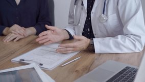 Doctor and patient sitting at the wooden table and discussing something. The pediatrician in a blue dotted blouse and white medical coat is gesturing actively. Medicine concept