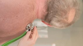 A female doctor listens to the work of the heart using a stethoscope. Vertical video.