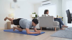 happy asian young man doing exercise and watching tutorial on laptop with mat in living room at home. Asia male doing workout woman watch television or tv . couple lifestyle at home .