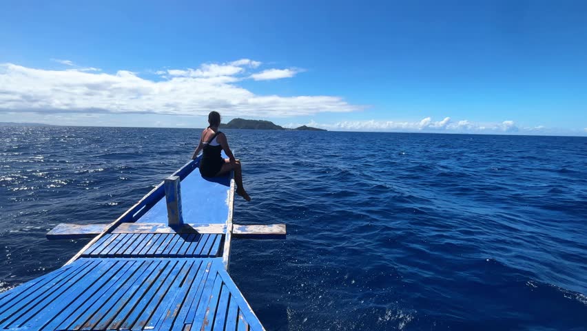 Girl sitting on the bow of a sailing boat on the ocean