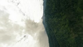 Vertical video. Aerial backward view green jungle forest erupting volcano frozen rocky lava slope gray smoke from crater. Environmental disaster. Wild nature mountains valley covering green plants 4k