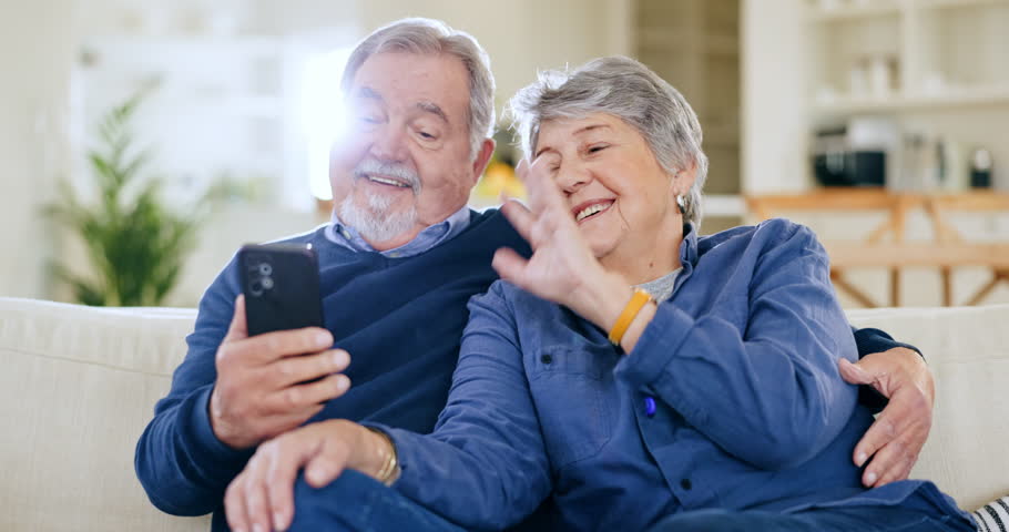 Elderly, wave and couple with phone for video call on sofa with hug, communication and happiness in living room. Senior, man and woman with smartphone on couch with greeting online for conversation