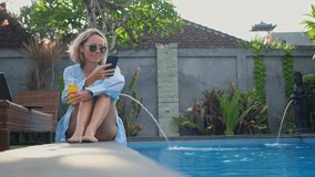 Mid adult woman calling on phone near the swimming pool at sunset time