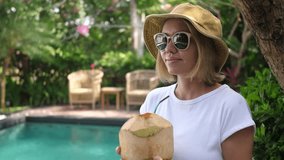 Female tourist with green coconut near the swimming pool, day shot