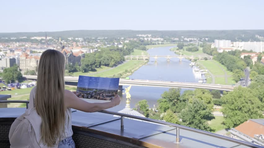 Tourist girl holding a map of the city of Dresden on the observation deck. Happy woman on vacation.