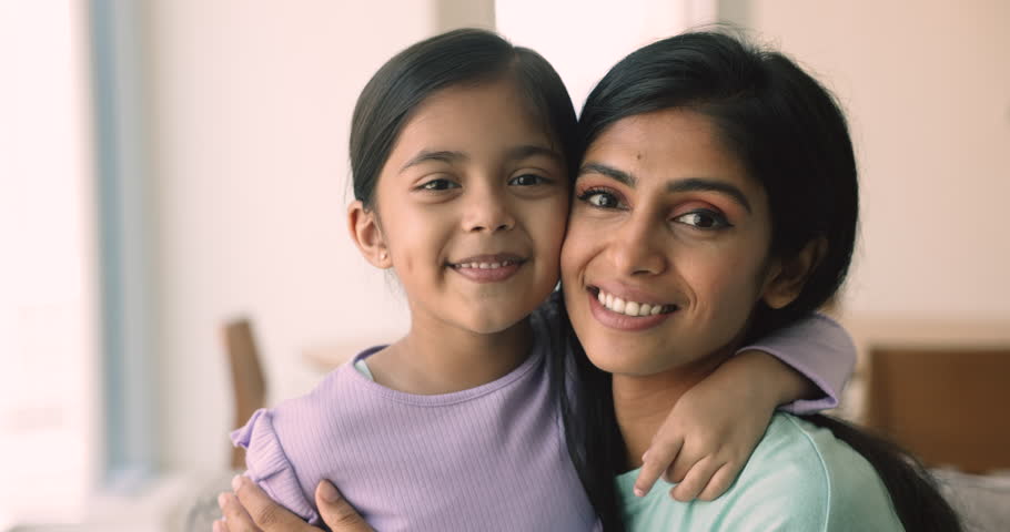 Close up shot of beautiful faces of young Indian mother cuddling her adorable little 5s daughter. Portrait of child hugs pretty mom smile looking at camera feel happy enjoy harmonic, loving relations Royalty-Free Stock Footage #1109599859